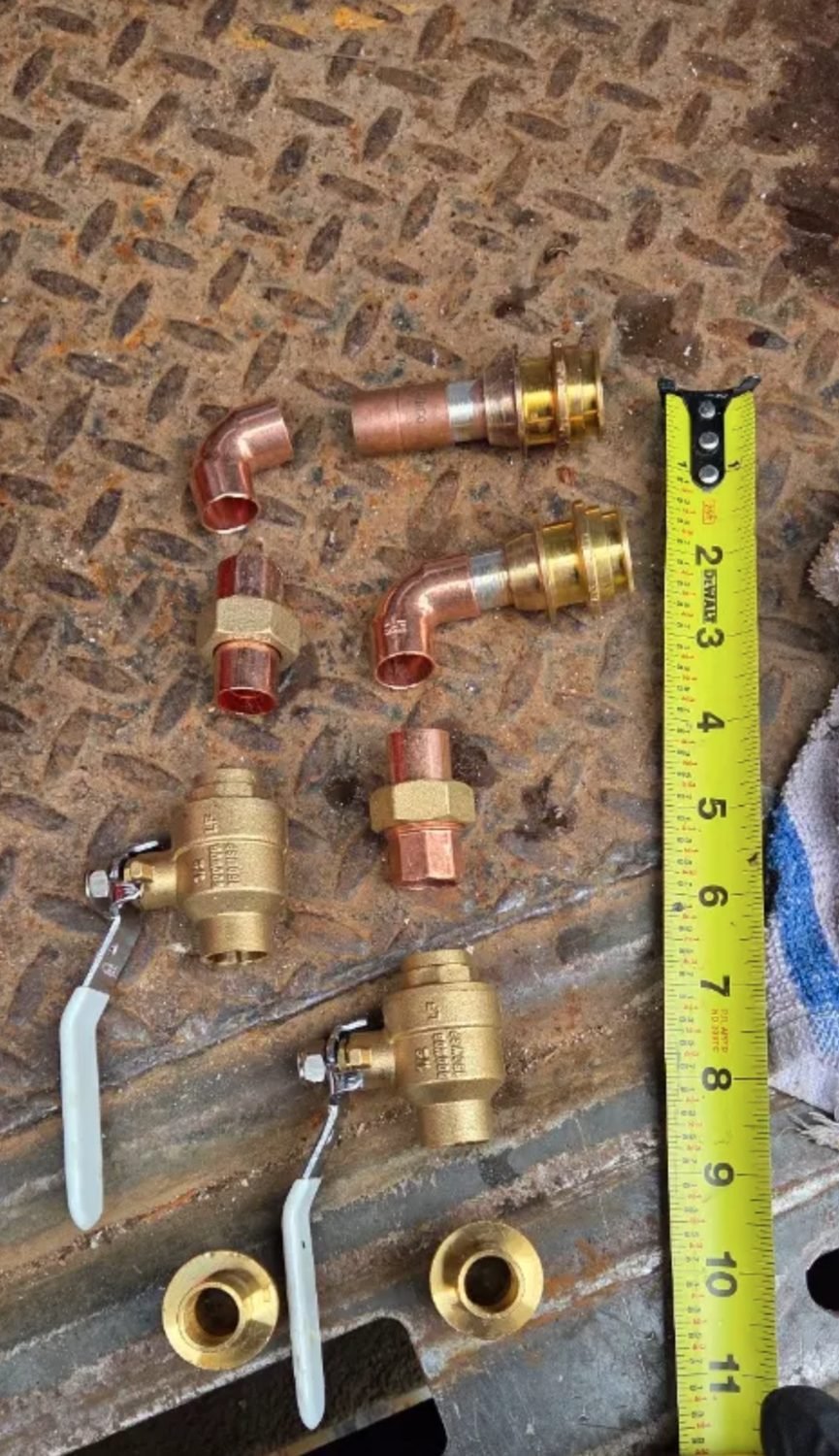 Brass ball valves and copper press fittings laid out against a tape measure