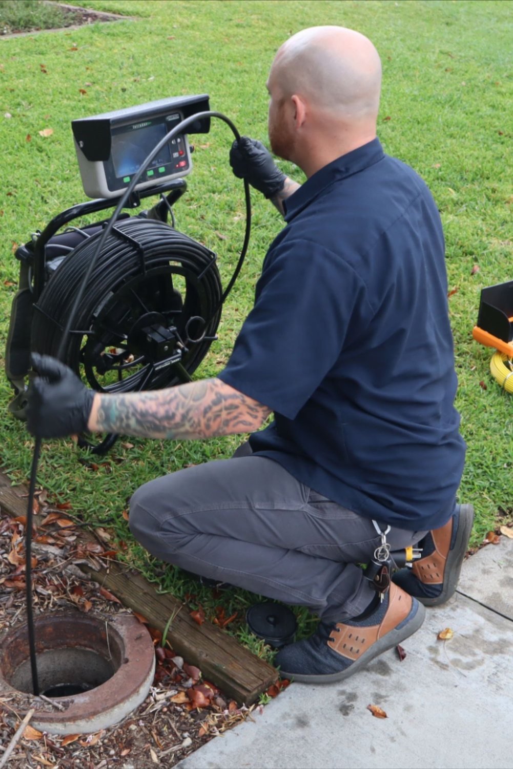Technician feeding a sewer camera into a cleanout at the edge of a lawn