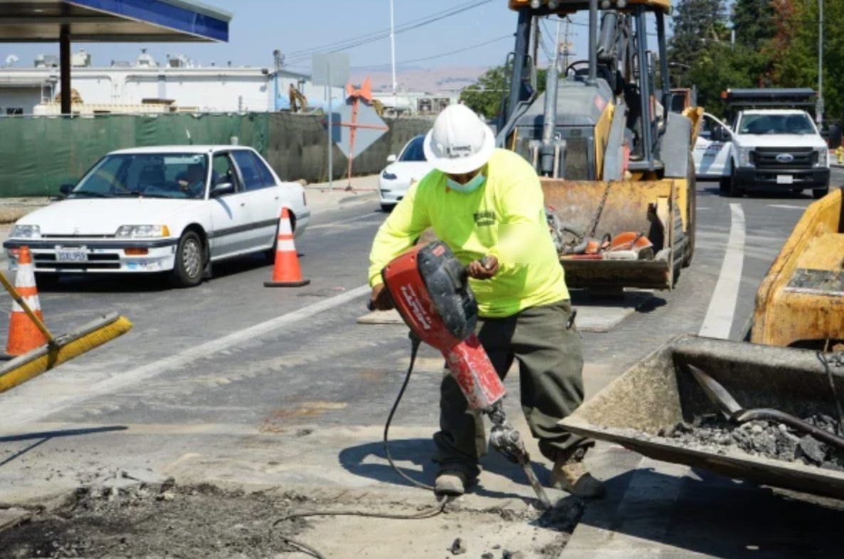 Worker using a jackhammer to break pavement over a buried line