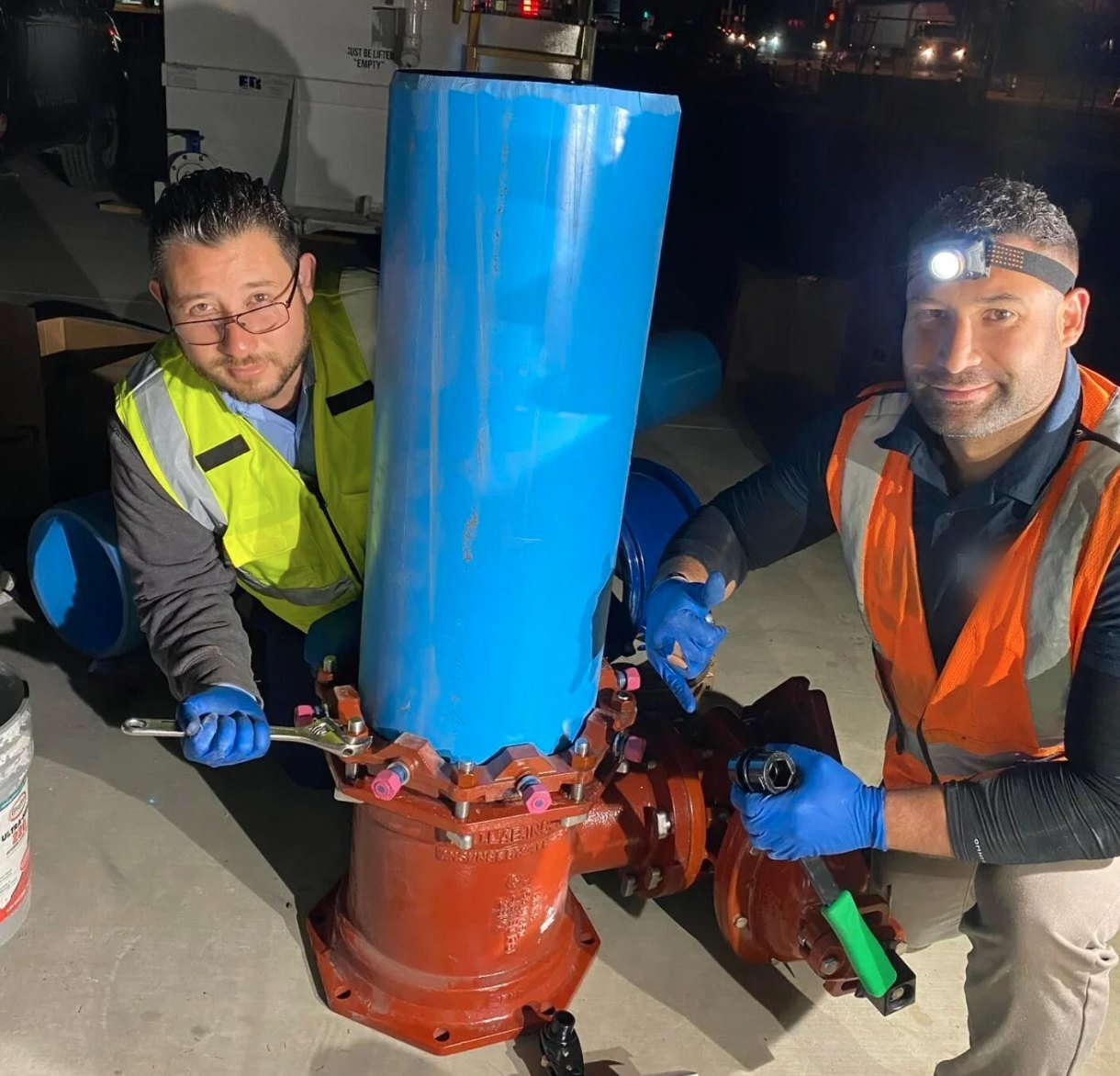 Two technicians in a trench alongside new pipe and a valve