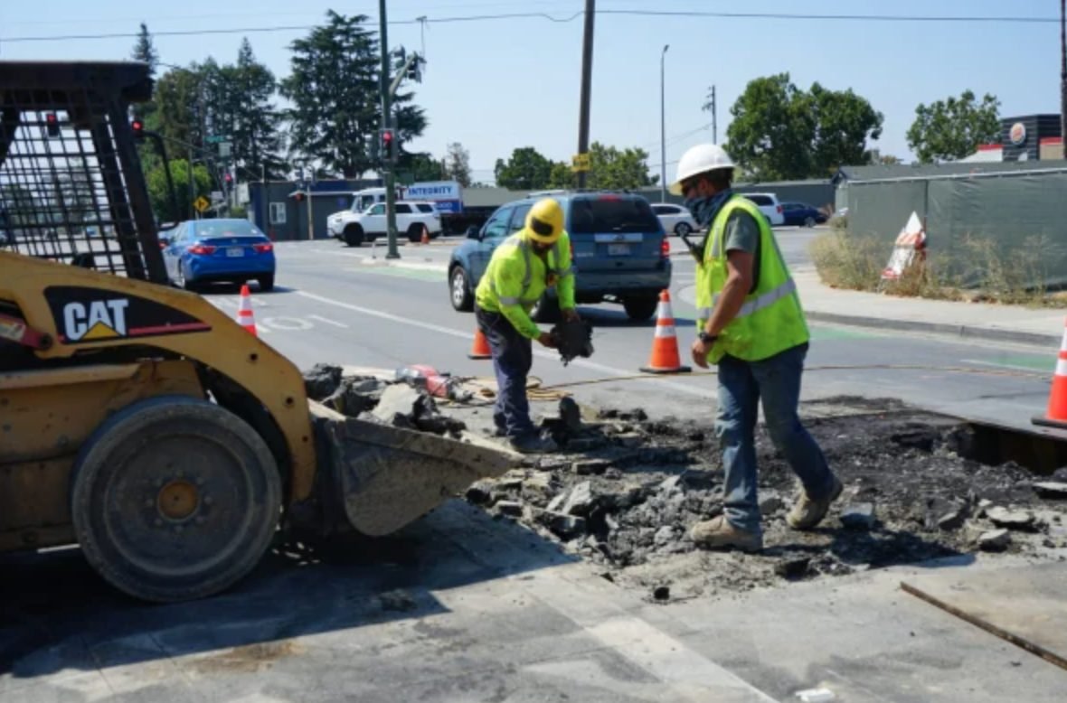 Workers breaking asphalt beside a skid steer loader