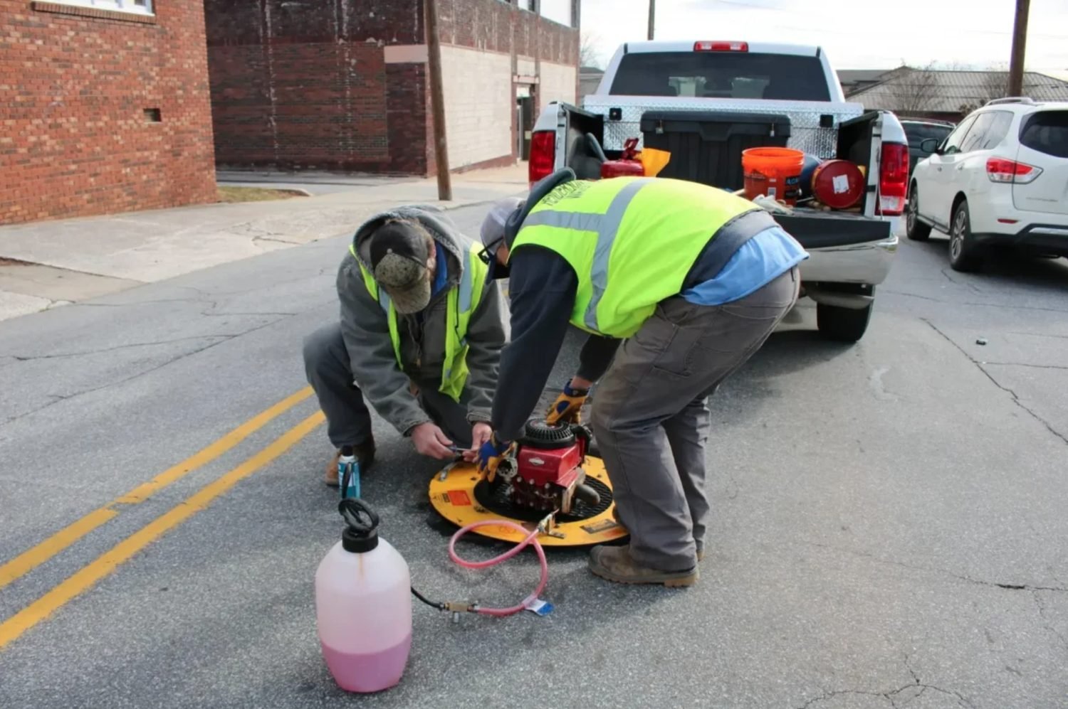 Technicians setting up a hydro jetting machine over a street access point
