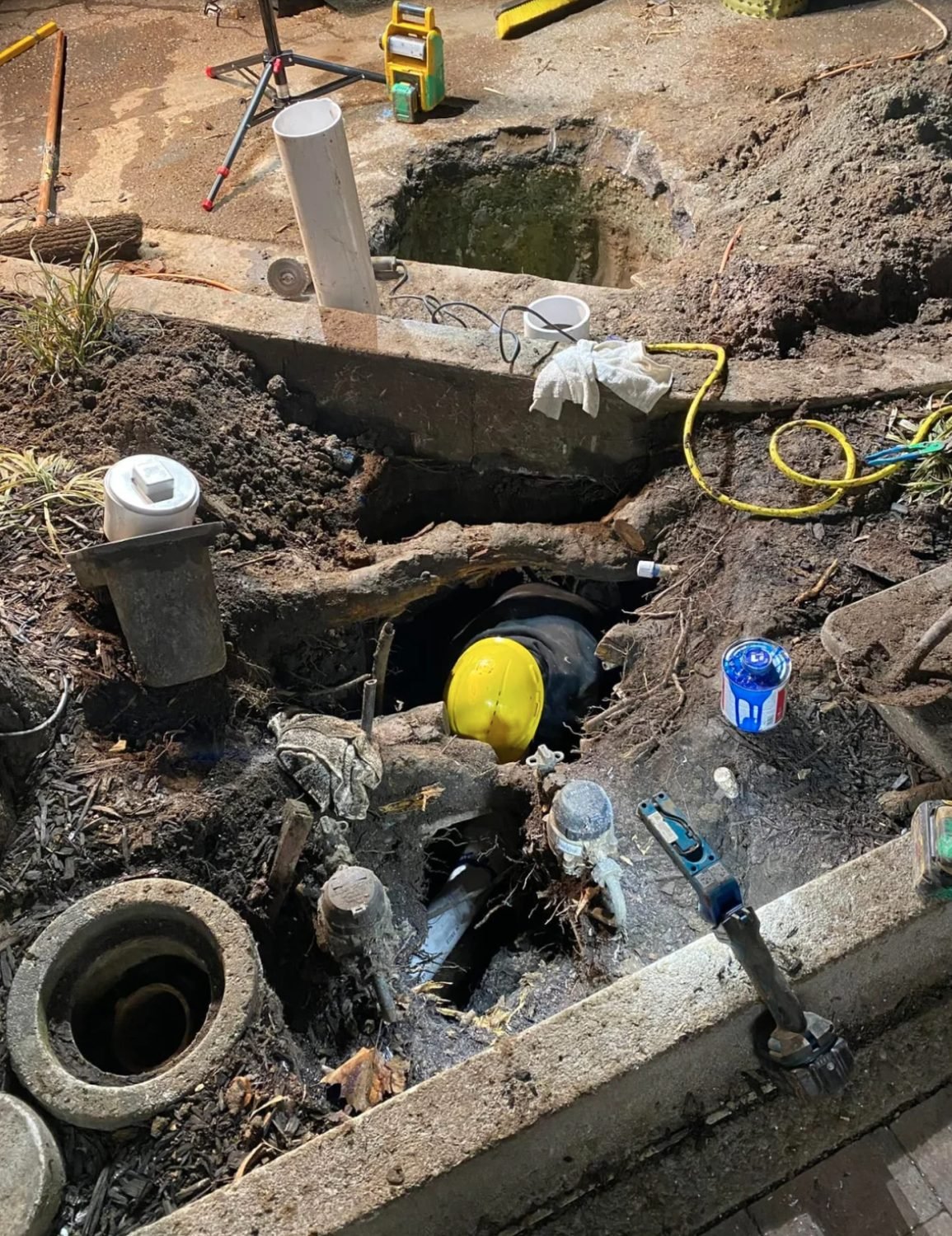 Open excavation at night exposing a sewer line and cleanouts