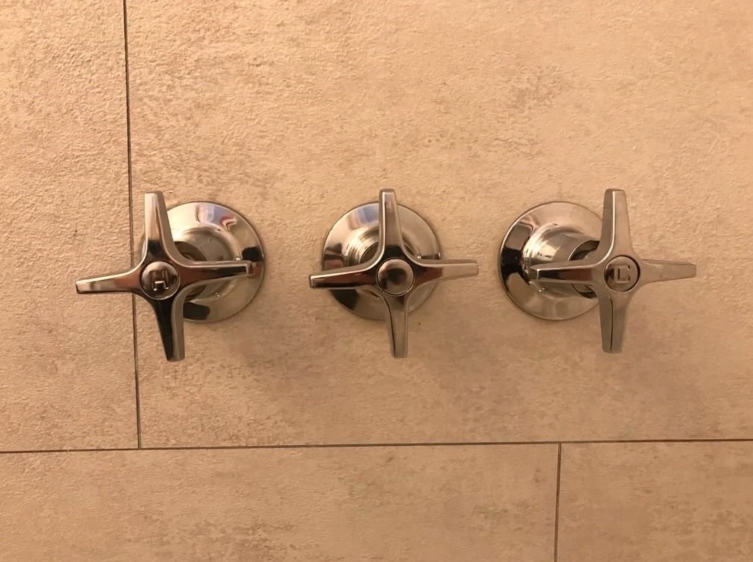 Three chrome shower valve handles installed on tile