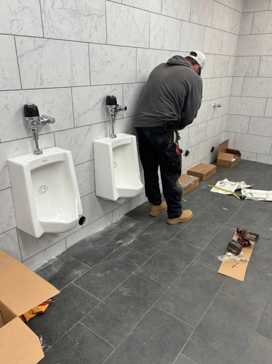 Technician installing wall hung urinals with flush valves in a commercial washroom