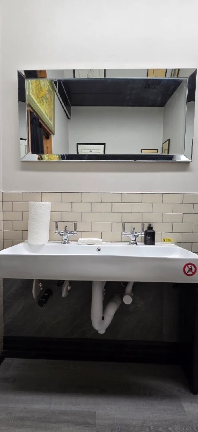 Finished commercial washroom with a trough sink, two faucets and a mirror