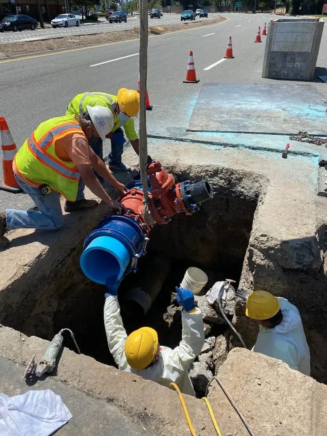Crew lowering a new valve assembly into a road excavation